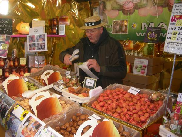 Vendor in BIO hat packs macarons into baskets at a market stall