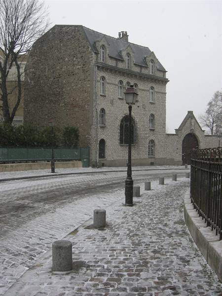 Snowy cobblestone street in front of a stone building with old lamppost