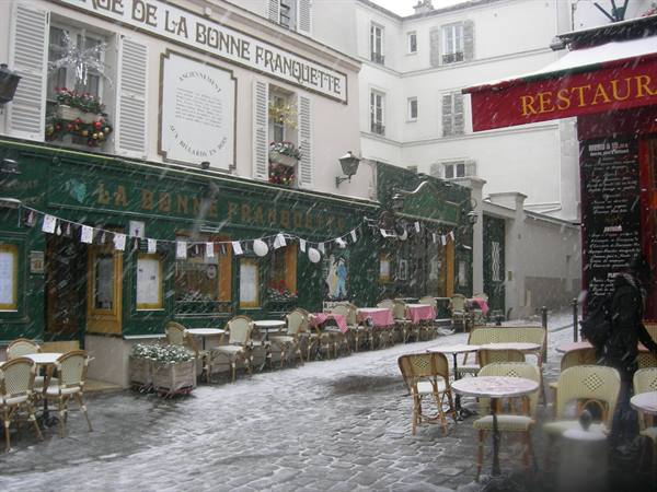 Snow falling on La Bonne Franquette restaurant, empty terrace chairs in Montmartre