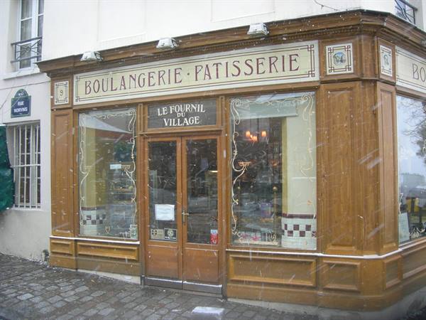 Wooden bakery on snowy cobblestone corner, Le Fournil du Village sign