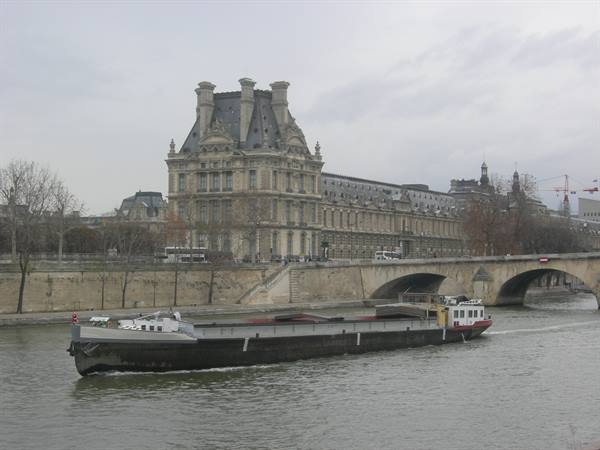 Barge sails on the Seine in front of the Louvre and a stone bridge