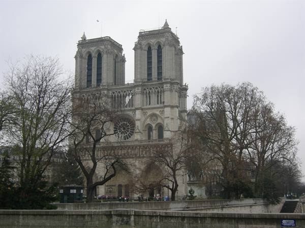 Notre-Dame cathedral among bare trees, grey sky, tourists by the Seine