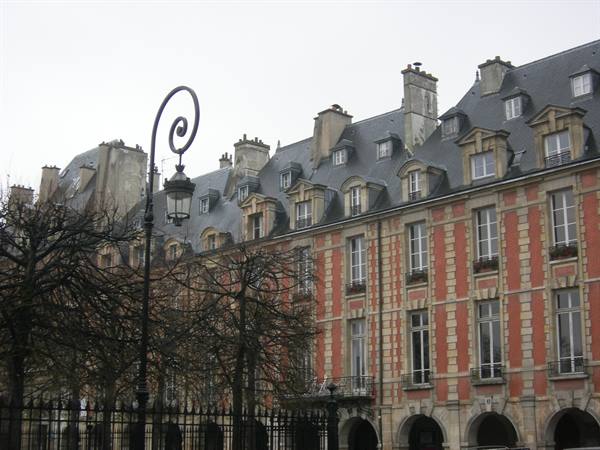 Red brick and stone facade of Place des Vosges, curved lamp post, bare trees