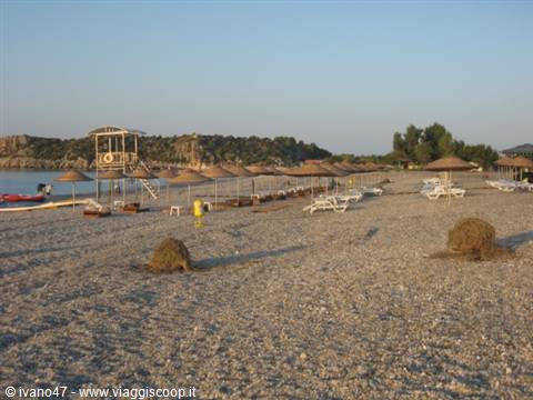 Pebble beach with straw umbrellas, empty sunbeds and wooden lifeguard tower