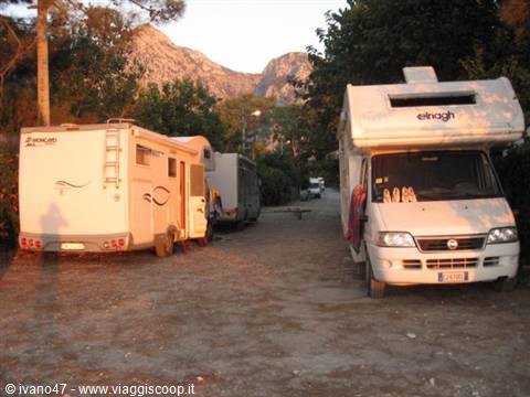Motorhomes and caravan parked on gravel, mountains glowing at dusk behind