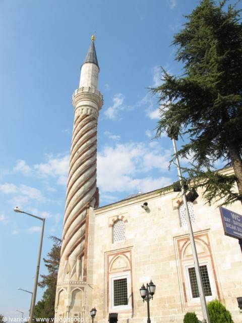 Stone minaret with red spiral pattern beside the mosque under a blue sky
