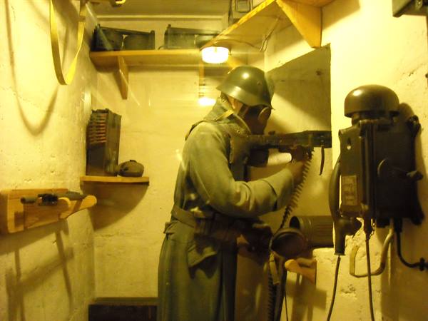 Soldier mannequin with helmet and gas mask, machine gun and telephone, inside a bunker