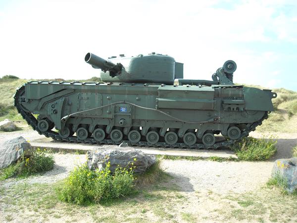 Green Churchill tank displayed on a plinth among rocks and wildflowers