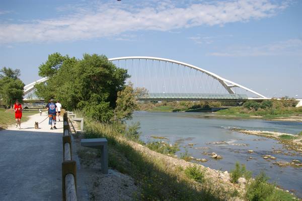 White arch bridge over the Ebro river in Zaragoza, cyclists along the bank