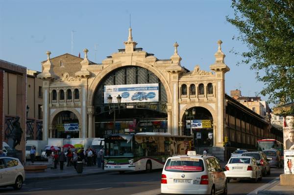 Central Market of Zaragoza, brick facade with large arch, buses and cars passing by