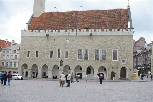 Tallinn's Gothic town hall with arches and tiled roof, tourists on the cobblestone square
