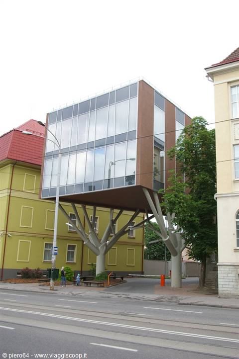 Glass building balanced on tree-shaped concrete pillars among colorful houses