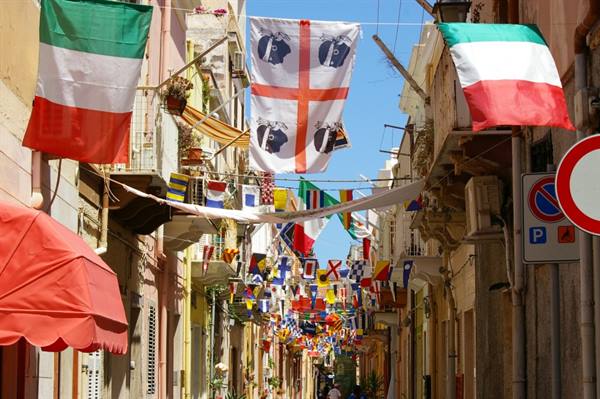 Italian and Sardinian flags strung between buildings along a festively decorated narrow street
