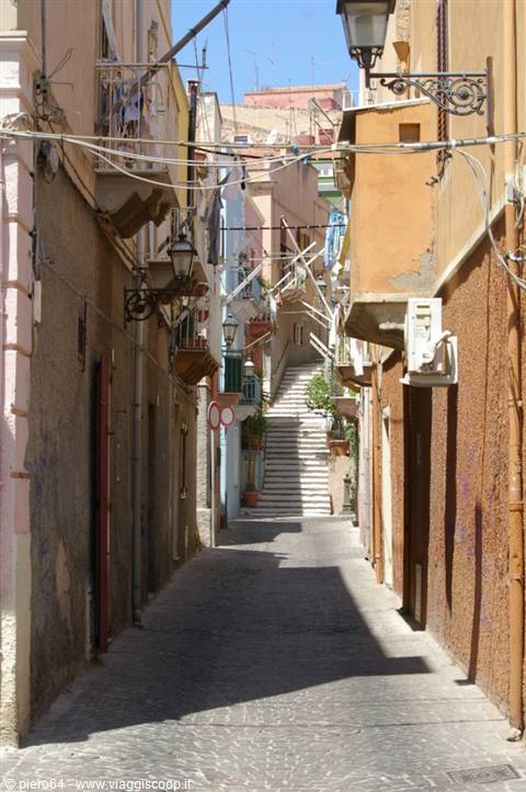 Steep alley with staircase between colorful houses, lanterns and laundry in sunlight