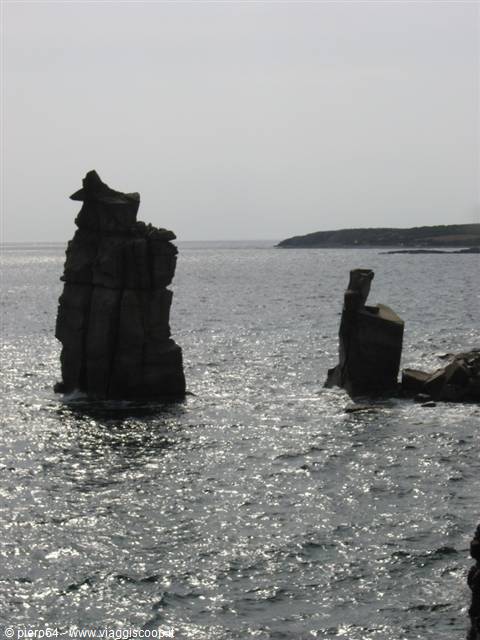 Black rock stacks rise from the sparkling sea under a grey sky