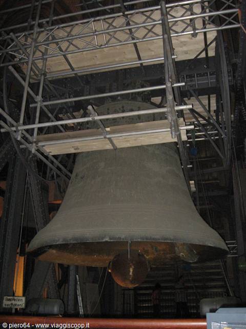 Huge bronze bell hanging among steel beams and scaffolding under artificial light