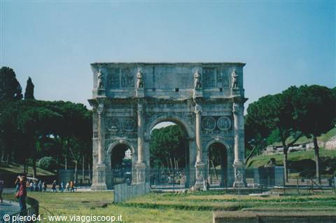 Tourists walk in front of the Arch of Constantine in Rome among pines and green grass