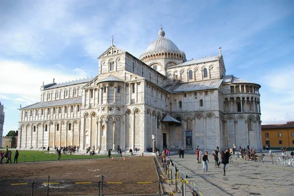 Tourists walk in front of Pisa Cathedral, white marble under a blue sky