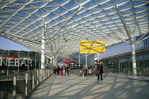 Travelers under the glass and steel lattice roof of Milano Garibaldi station