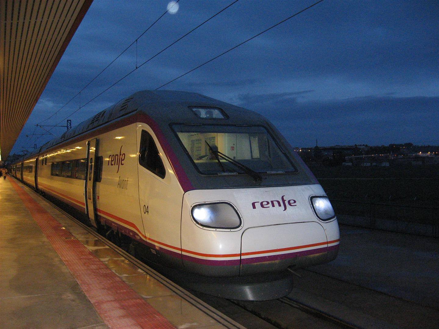 Treno Renfe fermo al binario della stazione la sera, fari accesi