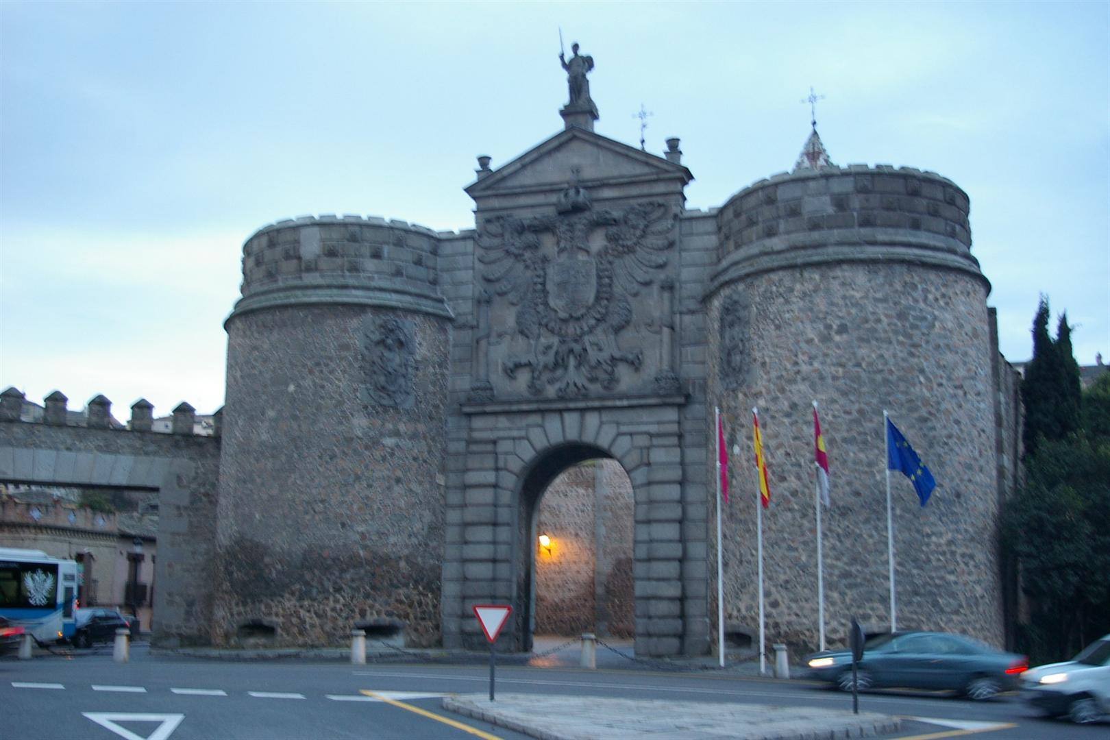 Porta Bisagra a Toledo: torri in pietra con lo stemma e statue, bandiere al vento