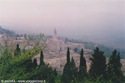 Assisi in the fog: stone houses, bell tower and cypresses in the foreground