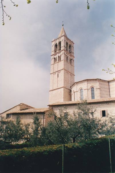 Pink stone bell tower of Santa Chiara Basilica in Assisi among olive trees