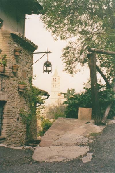 Stone alley with hanging lantern and Assisi bell tower among green trees