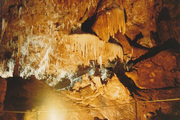 Stalactites and stalagmites lit by warm light in the cave, rope barrier below