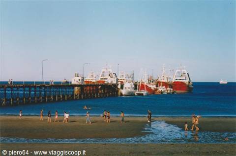 Beachgoers near the pier with red fishing boats at Puerto Madryn