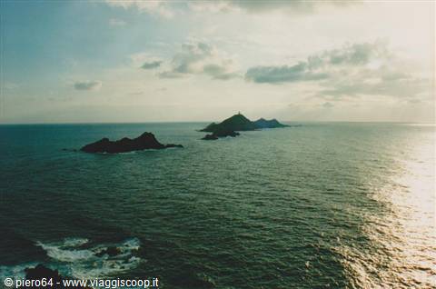 Dark islets rise from choppy sea, golden reflection on water, cloudy sky
