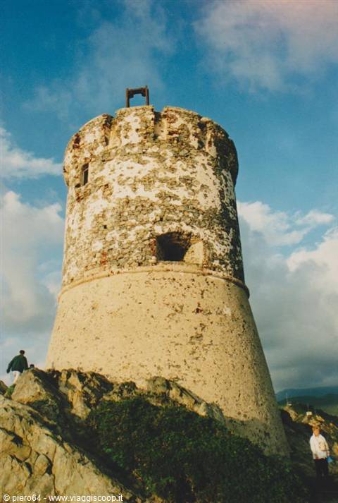 Old round stone tower on rocks, tourists climbing under cloudy sky