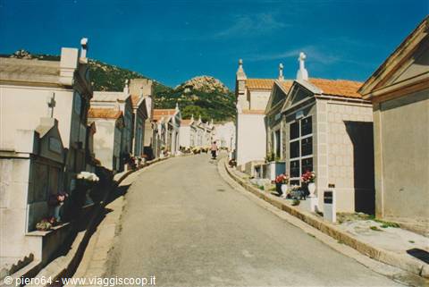 cemetery with masonry tombs along sloping road among granite rocks and blue sky