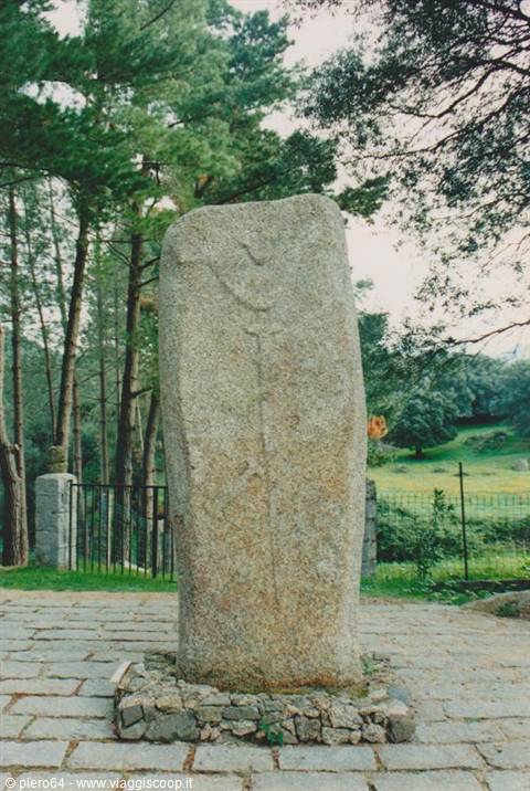 Granite menhir carved with a dagger, among pines and green meadow