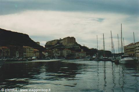 Sailboat entering Bonifacio harbour, citadel and cliffs under overcast sky