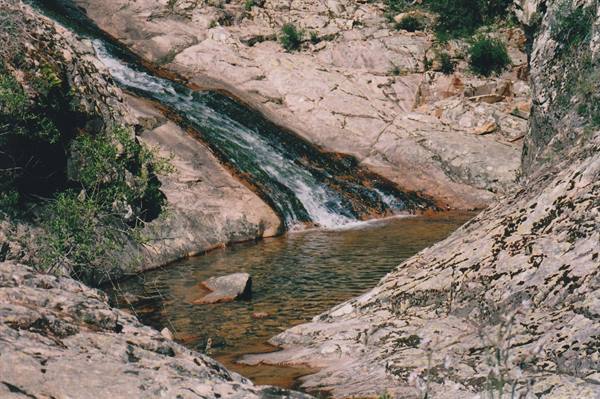 Small waterfall flows over granite rocks into a clear pool