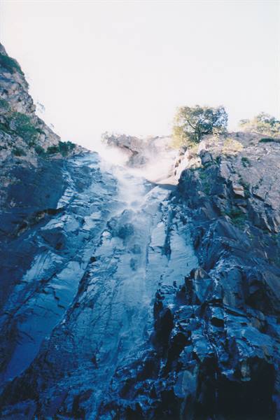 Waterfall cascading over wet rock between cliffs and trees