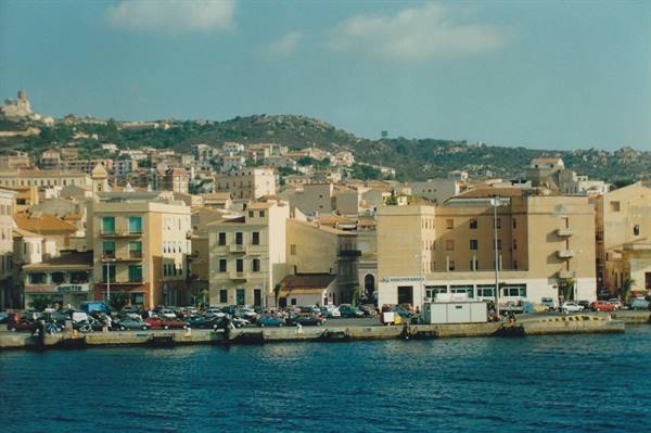 La Maddalena harbor: pastel buildings, parked cars, blue water and granite hills