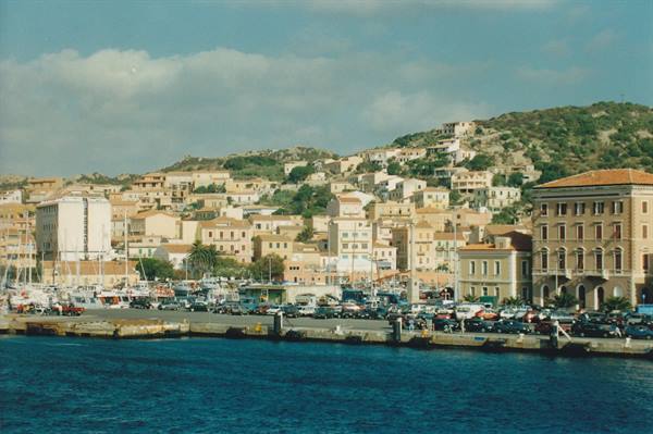 Harbor with moored boats, parked cars and colorful houses on sunny hillside