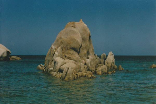 Large granite rock rising from turquoise sea beneath clear blue sky