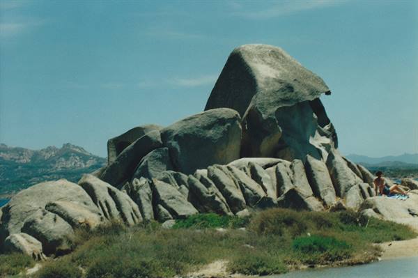 Huge turtle-shaped granite rock at Capo Testa, a tourist sitting nearby