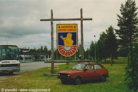 Red car parked under the wooden Arctic Circle sign at Napapiiri