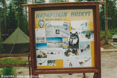 Wooden Napapiirin Huskyt signboard with sled dog photos beside a green tent