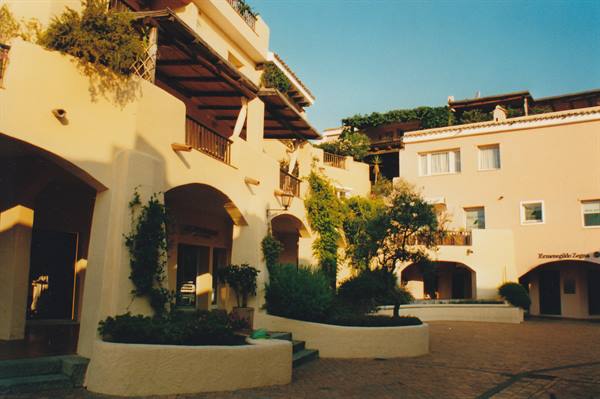 Small square with white arched buildings and climbing plants in warm morning light