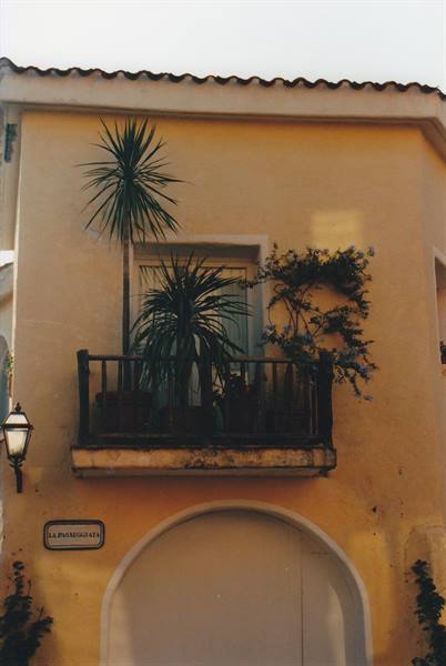 Wooden balcony with plants on yellow facade, lantern and sign