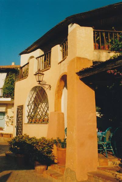 Mediterranean plastered building with arch, lattice window and lantern, flower pots, warm sunlight