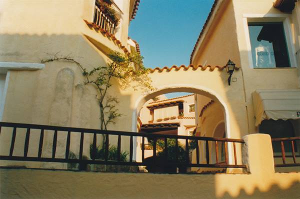 Yellow houses with brick arch and wooden railing in sunlight