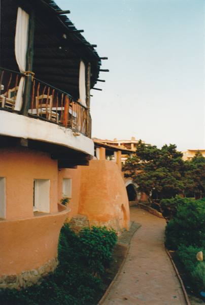 pink stucco building with wooden balcony and stone path among shrubs