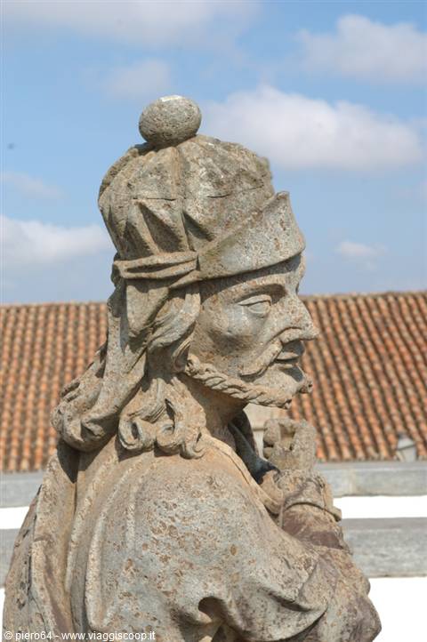 Stone statue of a crowned man, tiled roof and cloudy sky in background