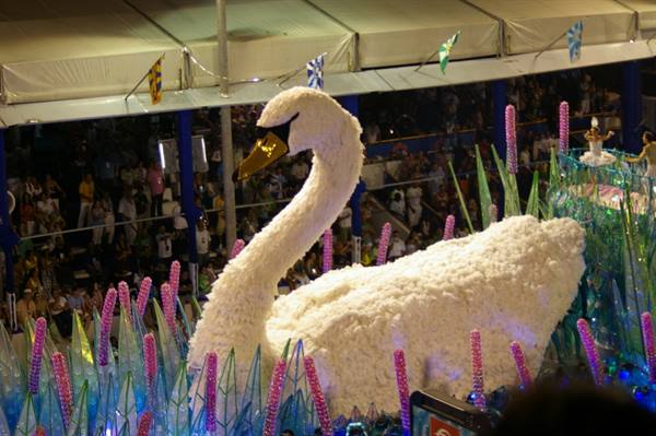 Carnival float shaped like a white swan among sparkling reeds, crowd below